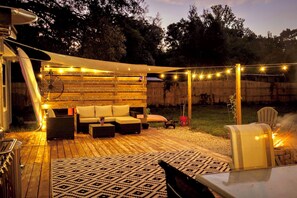 Ein Terrassenbereich im Freien mit Holzdeck, einer Sofagruppe, Lichterketten und einem Feuerkorb.