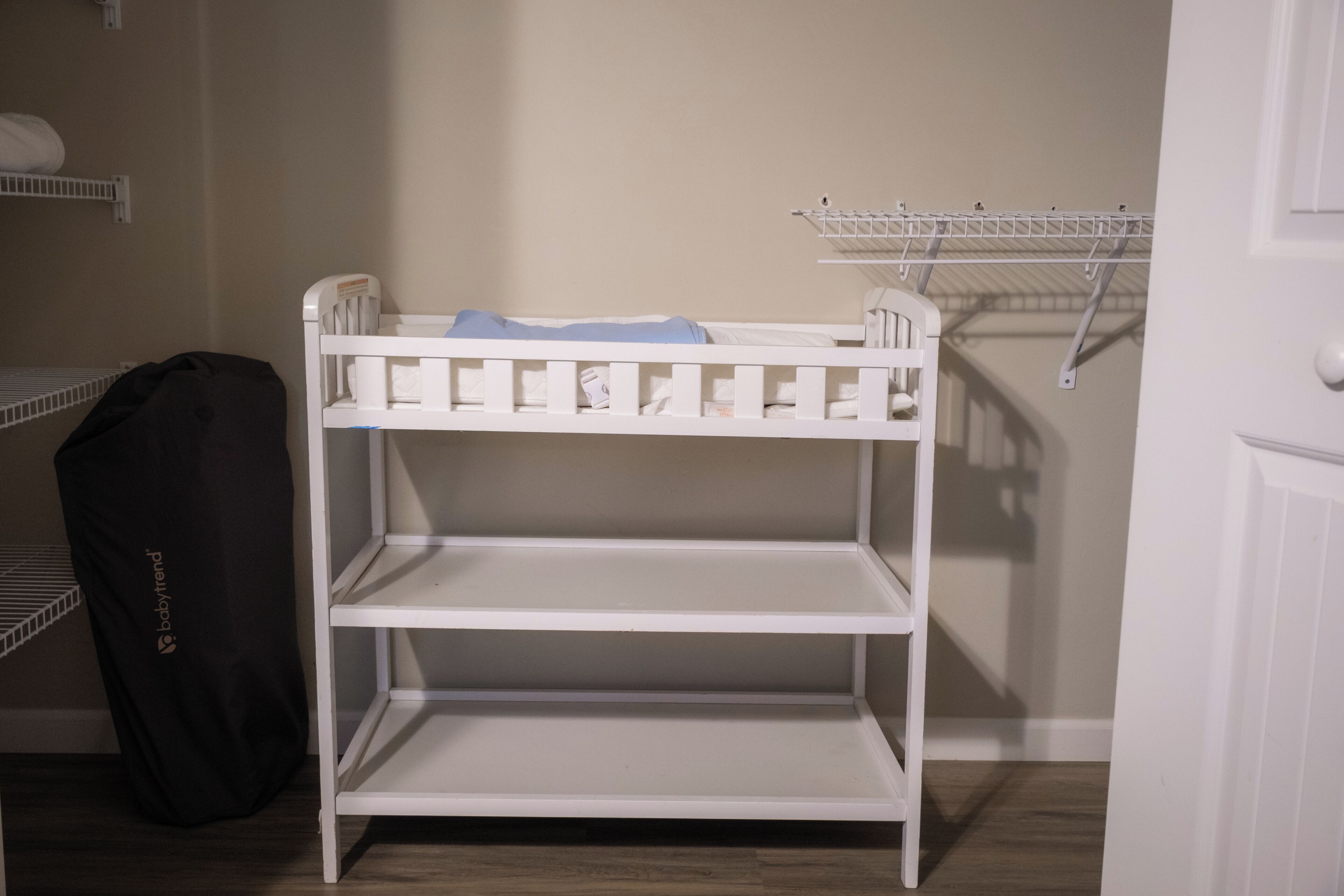 Een wit stapelbed met een plank, een zwarte tas en een witte deur.