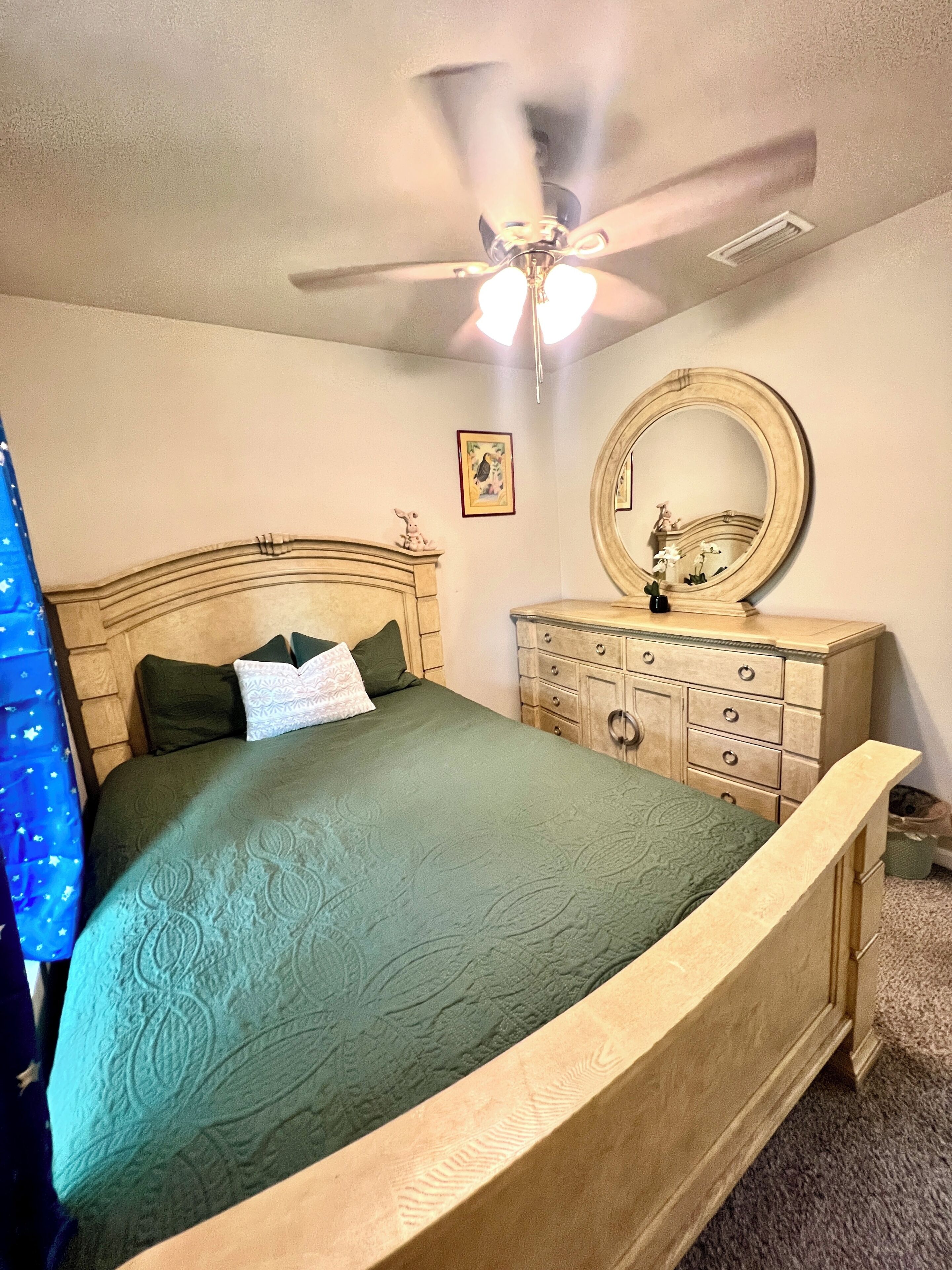 Een slaapkamer met een bed, een dressoir, een plafondventilator en een spiegel.