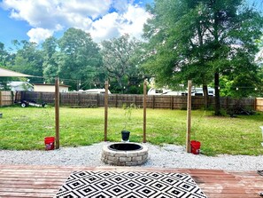 A backyard with a wooden deck, a fire pit, and a fenced area. - Min to the Springs• Fenced Yard • Fire Pit • Walk to Downtown • Pets (High Springs)