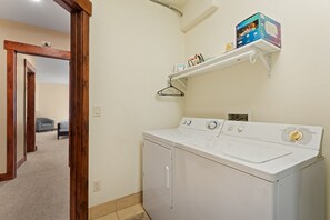 A laundry room with a front-loading washer and dryer, a shelf with laundry supplies, and a door leading to another room. - Spacious Wildernest Retreat with Private Hot Tub (Silverthorne)