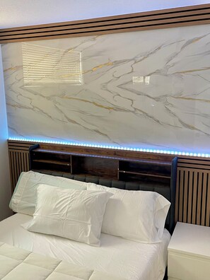 Una cama con ropa blanca y un cabecero con diseño de mármol.