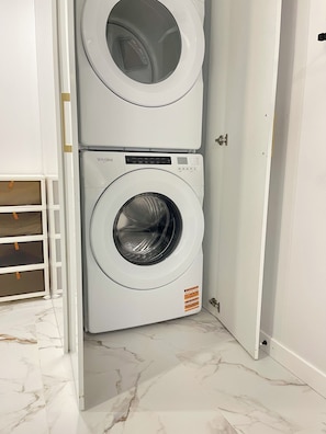 Uma máquina de lavar e secar Whirlpool compacta, de cor branca, num quarto com paredes brancas e soalho em mármore.