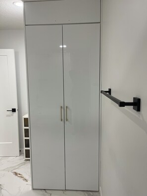 Een witte inbouwkast met twee deuren en een handgreep, een zwarte deurklink aan de muur, en een witte deur met handgreep op de achtergrond.