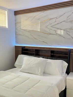 Quarto com uma cama, cabeceira com design que lembra mármore e uma janela com persianas.