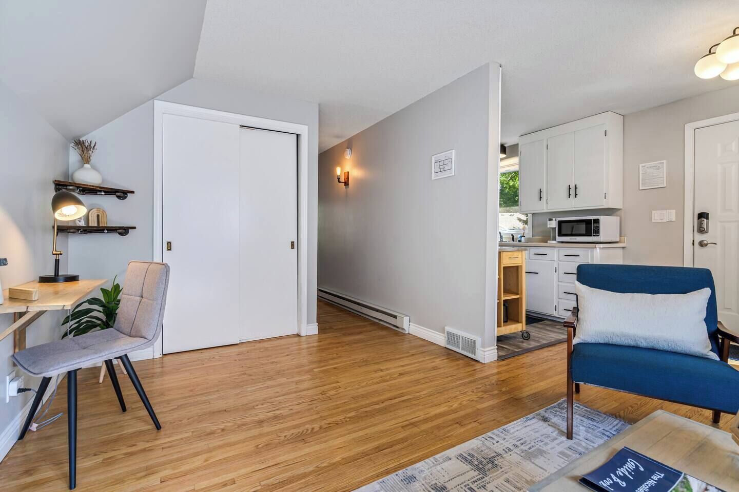 A modern apartment with a dining area, a blue sofa, a kitchen, and a white door.