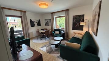 Un salon moderne comprenant un coin repas, des canapés verts, une table basse et des œuvres d’art accrochées aux murs.