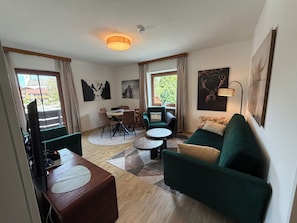 A modern living room with a dining area, green sofas, a coffee table, and artwork on the walls.