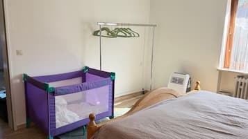 Ein Schlafzimmer mit einem Bett, einem violetten Babyreisebett, einem Heizkörper und einem Fenster.