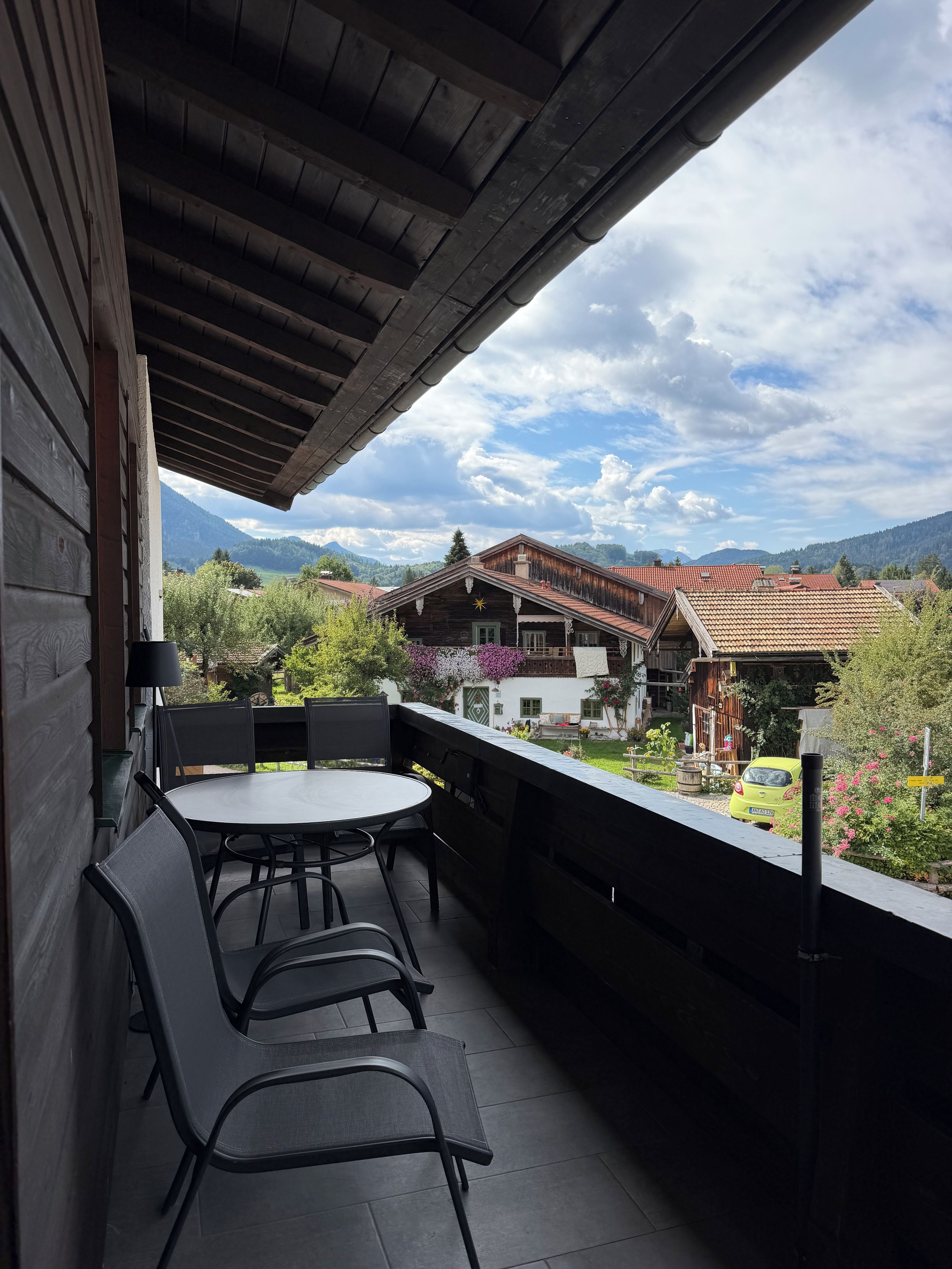 En balkon med et bord og stole, der kigger ud over et bjergrigt landskab med traditionelle bygninger.
