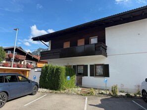 A building with a balcony, a parking sign, and a car.