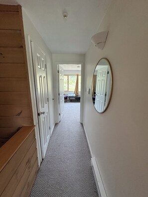 A hallway with a carpeted floor, wooden paneling on one side, and a mirror on the wall. - 4BR, 4 full bathroom condo, with community pool. Near Lake Michigan. (Cedar)