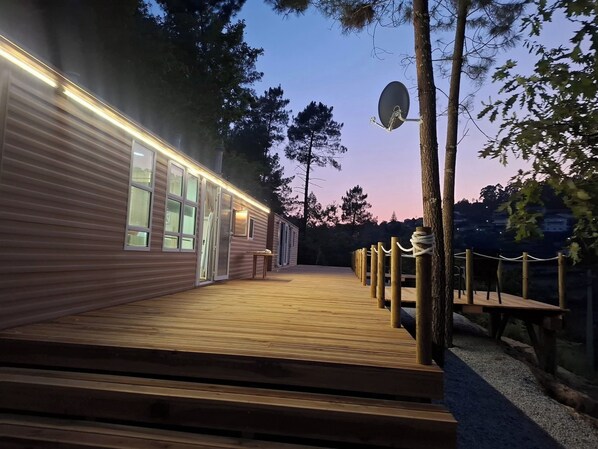 A wooden deck leading to a building with large windows and a satellite dish.