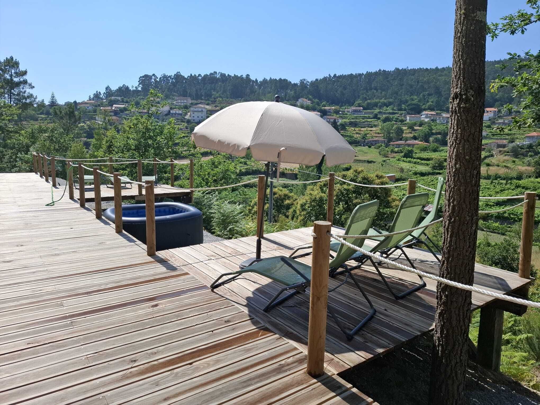 Um deck de madeira com vista para uma paisagem montanhosa, uma piscina insuflável redonda e alguns cadeiras de descanso.