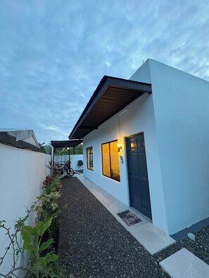 A modern house with a covered patio, a gravel pathway, and a door with a light fixture. - Vacation home with a private pool and close to the beach (Jacó)