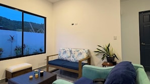 A modern living room with a large window, a sofa, a chair, and a coffee table. - Vacation home with a private pool and close to the beach (Jacó)