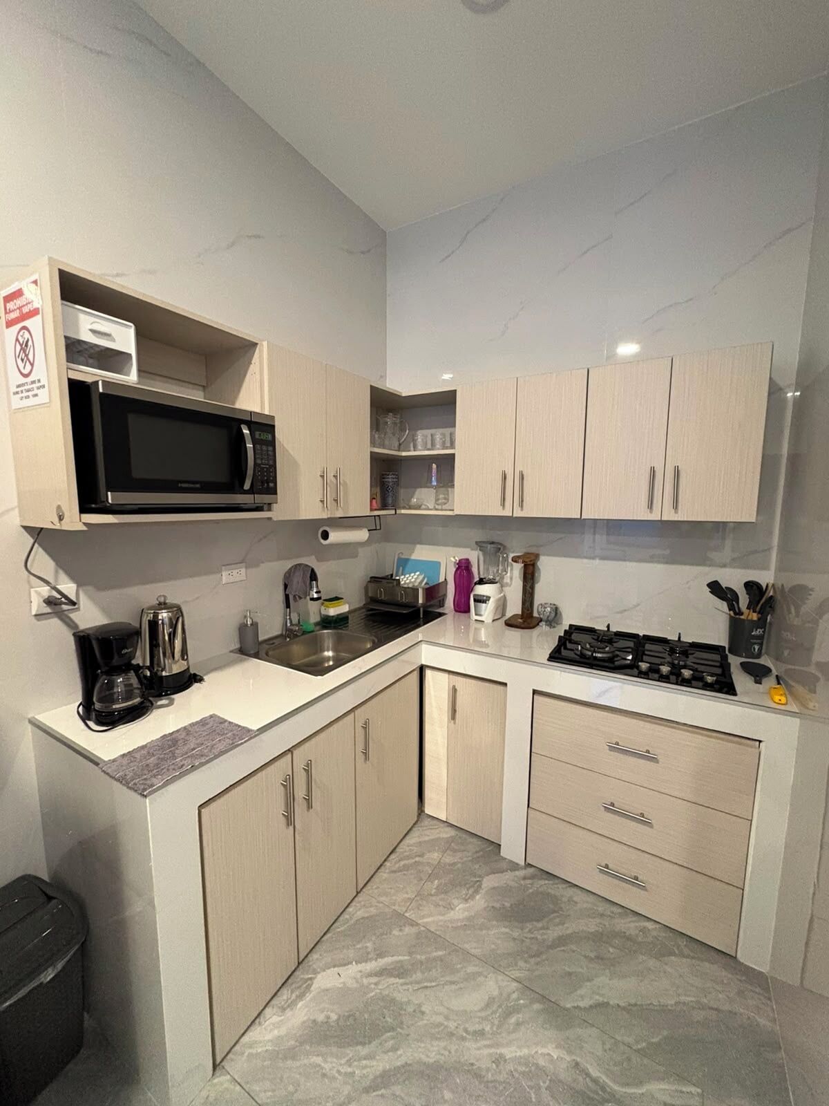 Een kleine keuken met een magnetron, koffiezetapparaat, spoelbak en gasfornuis.