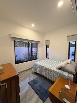 A bedroom with a bed, bedside table, and a window with a view of greenery. - Vacation home with a private pool and close to the beach (Jacó)