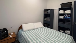 A bedroom with a bed, a nightstand, a lamp, and built-in shelving with folded clothes. - Vacation home with a private pool and close to the beach (Jacó)