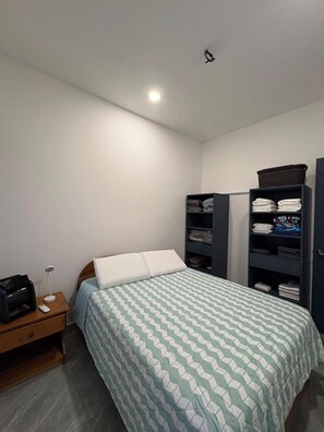 A bedroom with a bed, a nightstand, a lamp, and built-in shelving with folded clothes. - Vacation home with a private pool and close to the beach (Jacó)