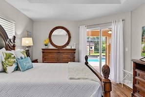 A bedroom with a bed, a dresser, a mirror, and a view of a pool. - Sea Your Escape | Pool, Game Room & Lanai | Palm Coast Near Flagler Beach (Palm Coast)