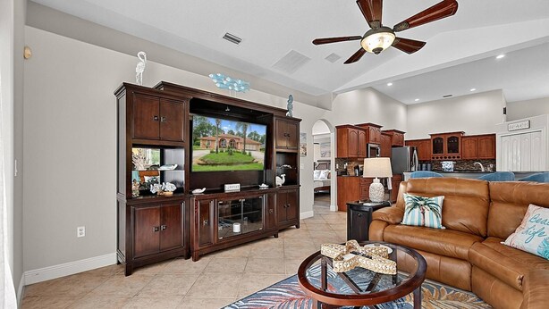 A living room with a television, leather sofa, and a ceiling fan. - Sea Your Escape | Pool, Game Room & Lanai | Palm Coast Near Flagler Beach (Palm Coast)