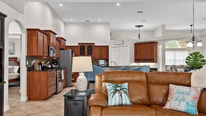 A spacious living area with a brown leather sofa, a kitchen with wooden cabinets, and a dining area with a table and chairs. - Sea Your Escape | Pool, Game Room & Lanai | Palm Coast Near Flagler Beach (Palm Coast)