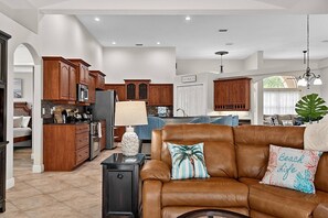 A spacious living area with a brown leather sofa, a kitchen with wooden cabinets, and a dining area with a table and chairs. - Sea Your Escape | Pool, Game Room & Lanai | Palm Coast Near Flagler Beach (Palm Coast)
