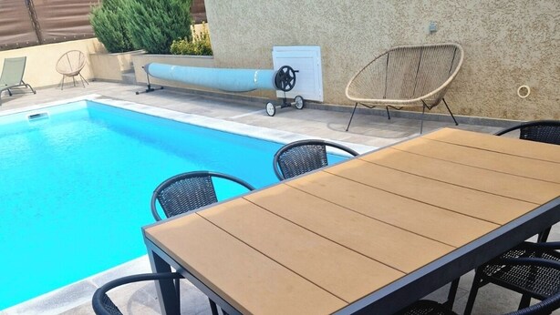 Ein Poolbereich im Freien mit Holztisch und -stühlen, einer Liege und einem kleinen Wasserspiel.