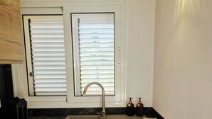 Eine Küche mit Spüle, Holzschränken, einem Fenster mit Jalousien und einer Wandleuchte.