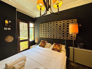 Un dormitorio con una cama grande, dos lámparas de noche, un panel decorativo en la pared y un ventanal con vistas.
