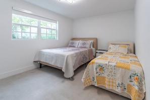 Une chambre avec deux lits, une grande fenêtre et une vue sur la verdure.