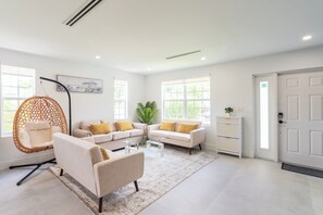A modern living room with a sofa set, a hanging chair, a glass coffee table, and a potted plant. - NEW 3BR • 7 Beds • Sleeps 12+ • Free Parking (West Palm Beach)