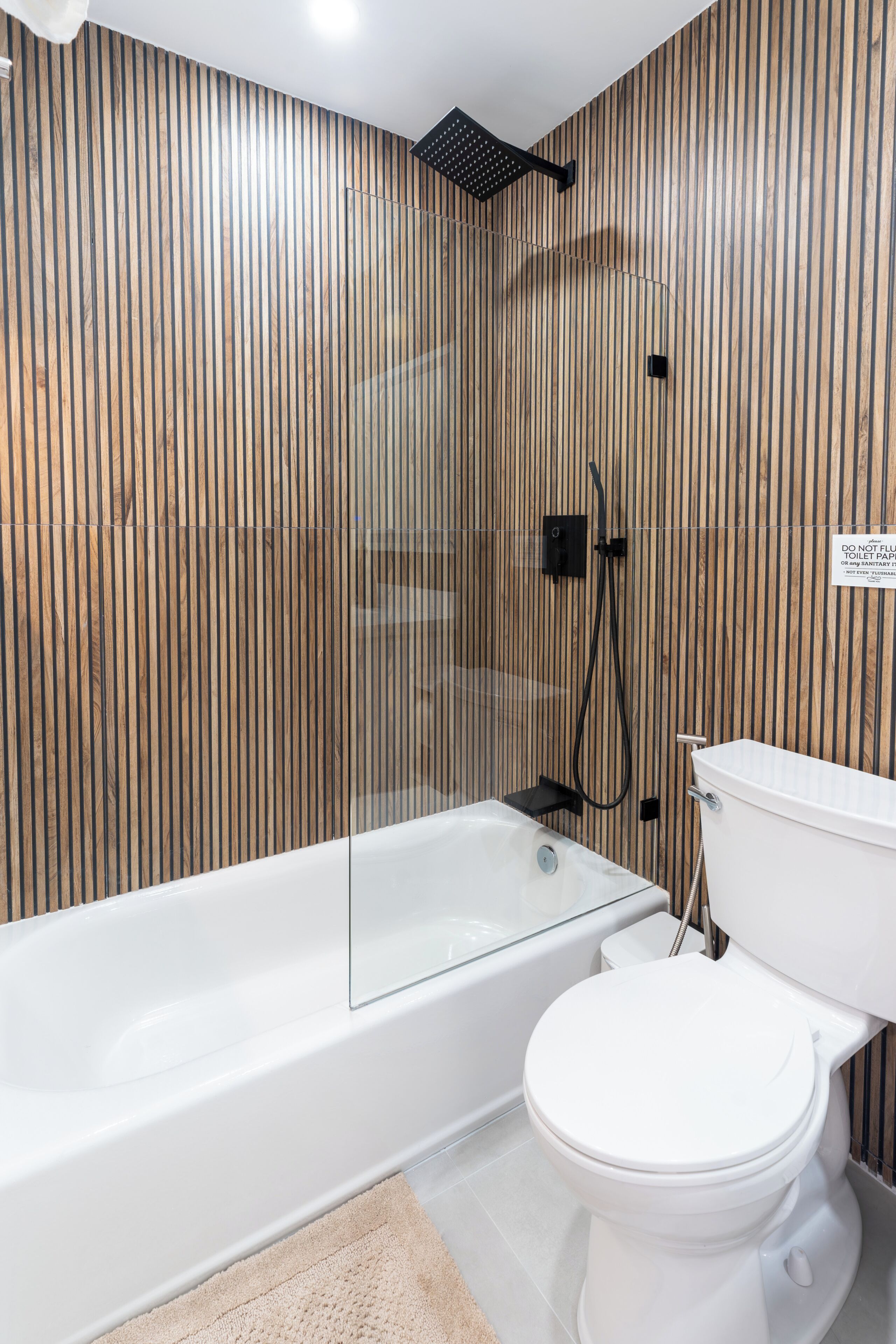 Ein modernes Badezimmer mit einer Wand aus Holzlamellen, einer Duschkabine aus Glas und einer weißen Toilette.