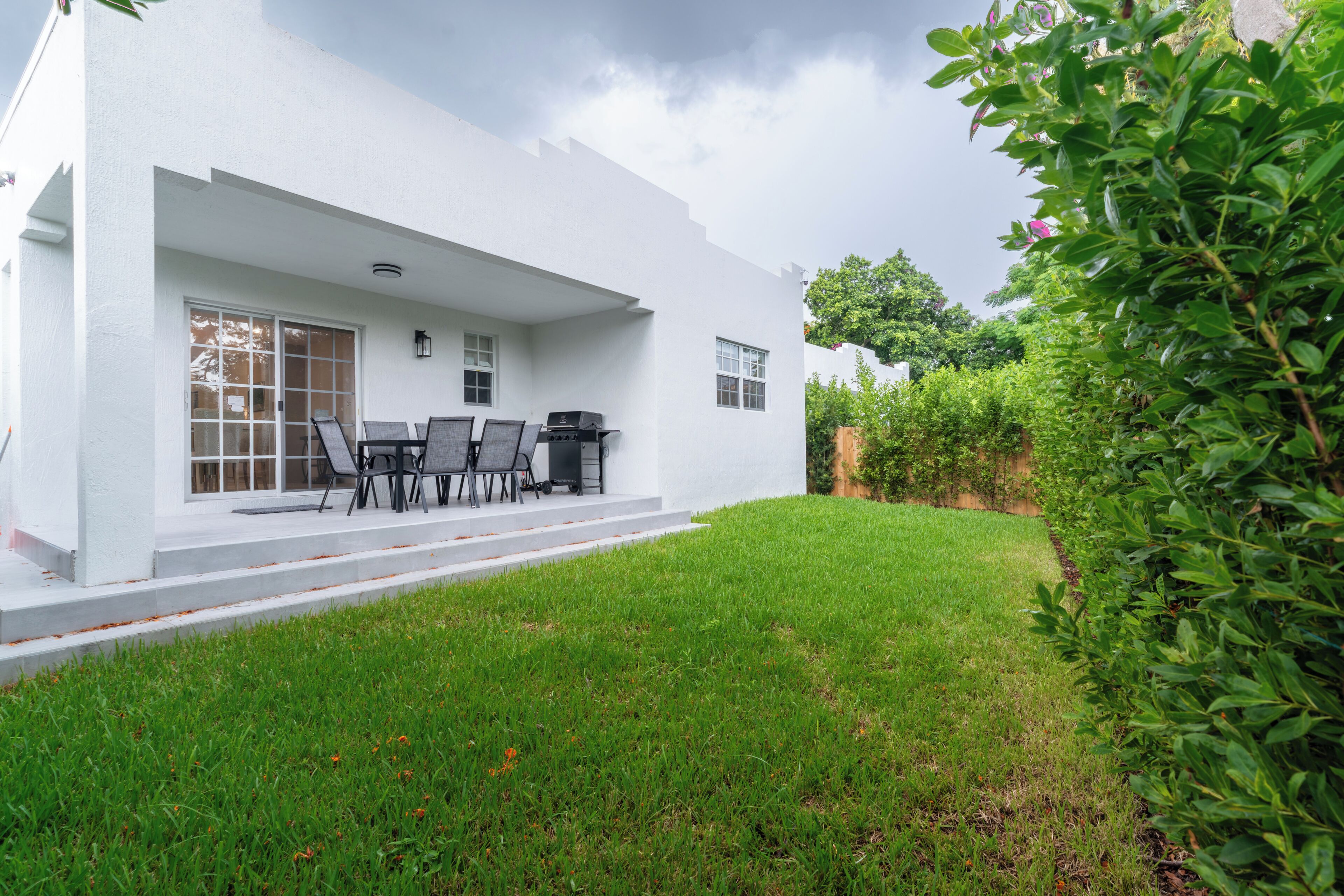 A white house with a covered patio, outdoor seating, and a well-maintained lawn.