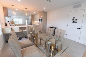 A modern kitchen with stainless steel appliances, a dining area with a glass table and cushioned chairs, and a laundry symbol on the wall. - NEW 3BR • 7 Beds • Sleeps 12+ • Free Parking (West Palm Beach)