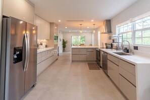 A modern kitchen with stainless steel appliances, a large island, and a view of the outdoors. - NEW 3BR • 7 Beds • Sleeps 12+ • Free Parking (West Palm Beach)
