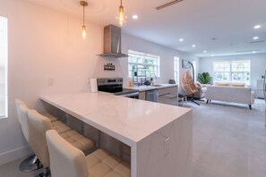 A modern kitchen with a marble island, built-in oven, and a hanging light fixture. - NEW 3BR • 7 Beds • Sleeps 12+ • Free Parking (West Palm Beach)
