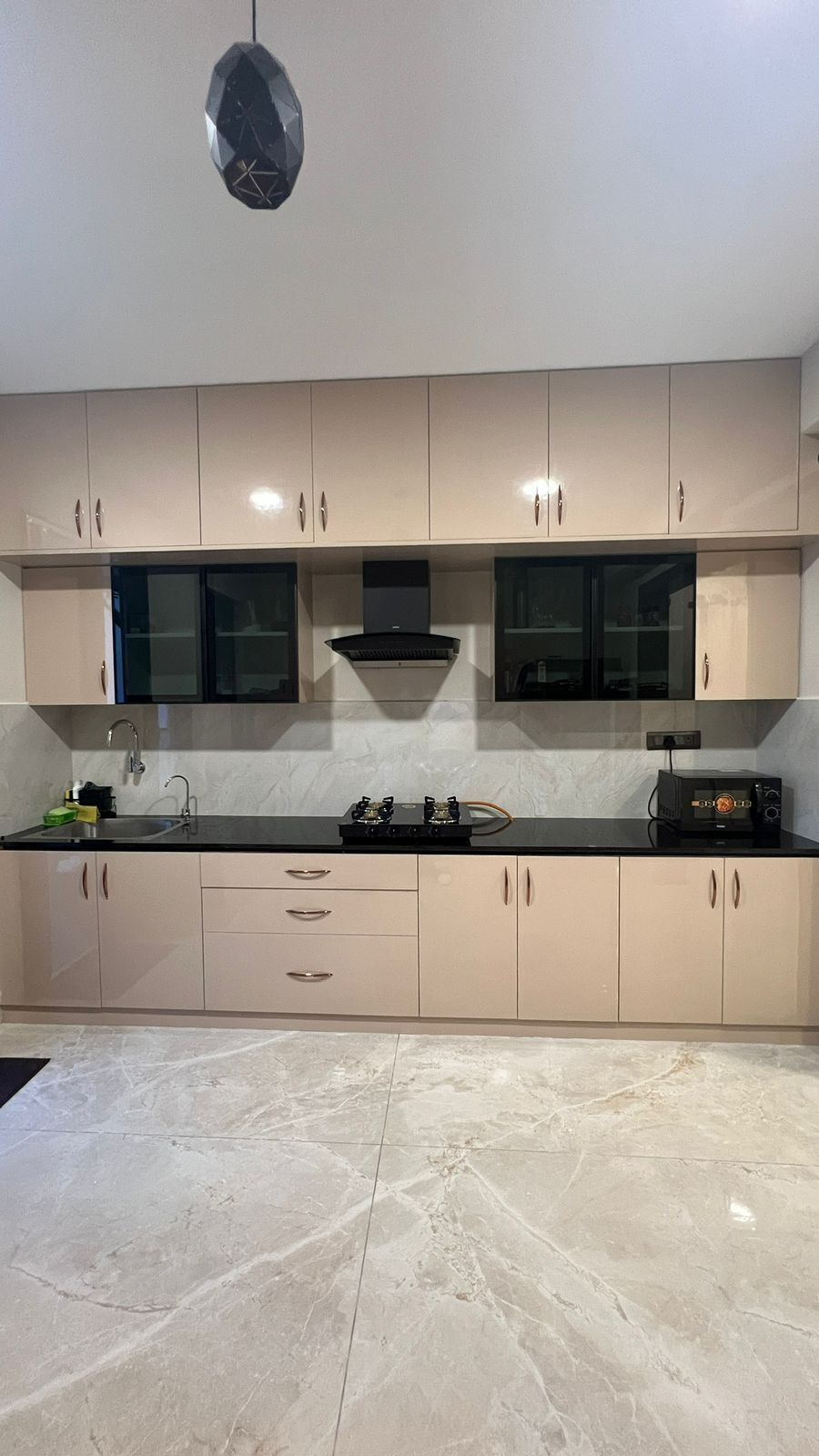 A modern kitchen with beige cabinets, a black countertop, and a marble floor.