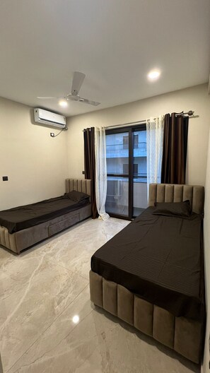 A bedroom with two beds, a ceiling fan, an air conditioning unit, and a sliding glass door to the outside. - Aureum Park Residence Spacious Family-Friendly 3BHK Near CBD & MG Road (Bengaluru)