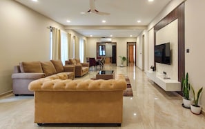 A spacious living area with a large sofa, a dining table with chairs, and a flat-screen TV mounted on the wall. - Aureum Park Residence Spacious Family-Friendly 3BHK Near CBD & MG Road (Bengaluru)