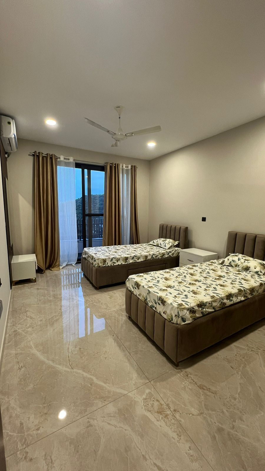 A hotel room with two beds, a ceiling fan, a window with curtains, and a view of the city.