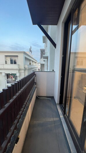 A narrow balcony with a dark-colored railing, a glass door, and a clear view of the street and buildings in the background. - Aureum Park Residence Spacious Family-Friendly 3BHK Near CBD & MG Road (Bengaluru)