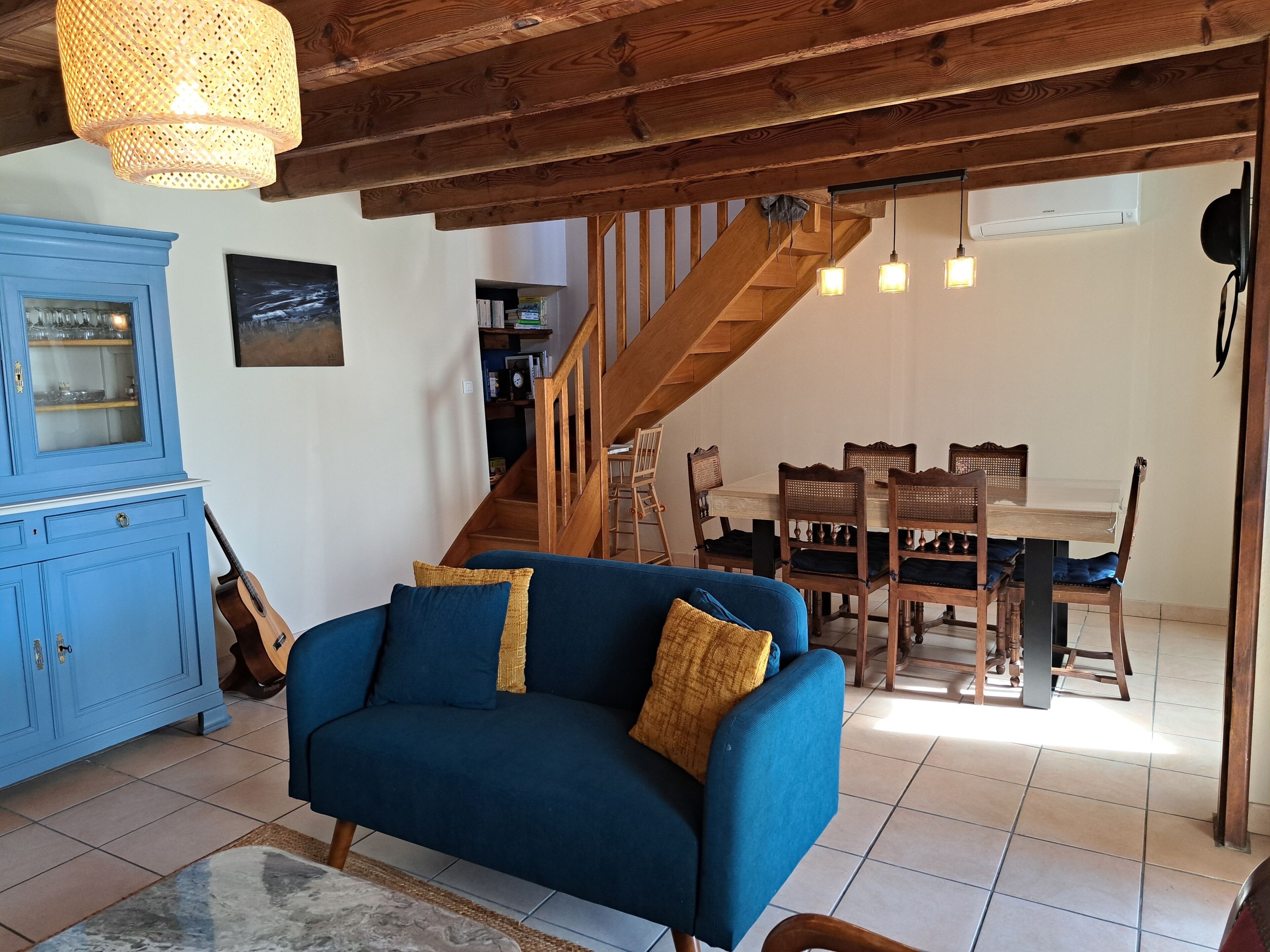 A living room with a blue sofa, wooden dining table, and a staircase leading to an upper level.