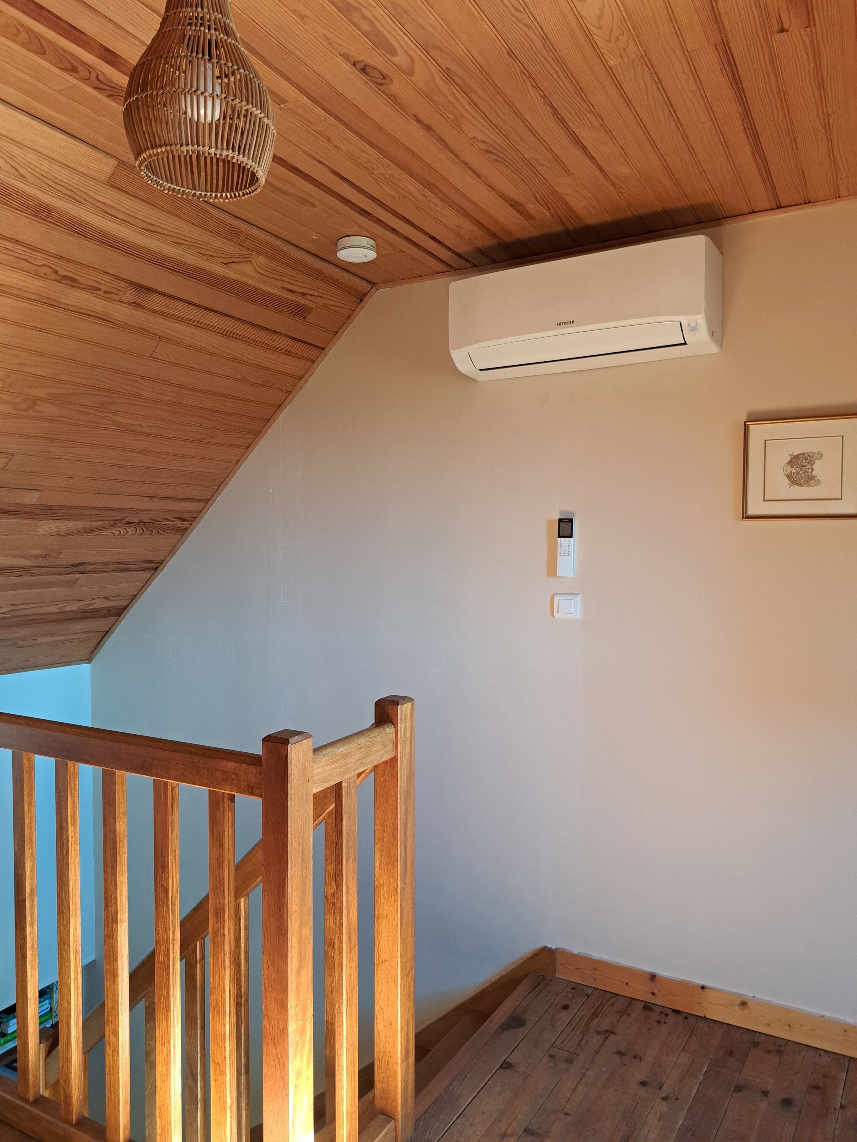 A wooden staircase with a railing, an air conditioning unit mounted on the wall, and a framed picture.