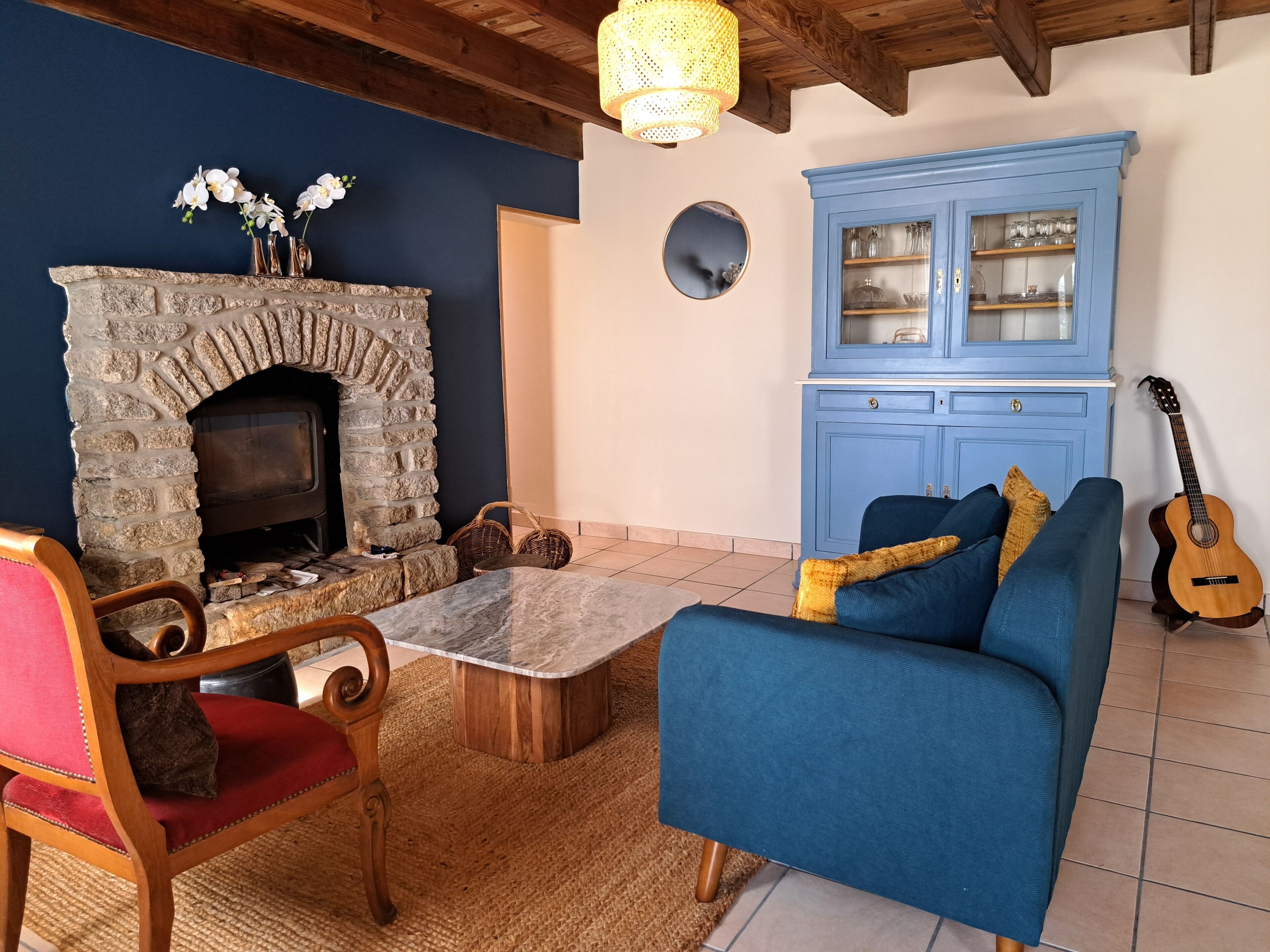 Una sala de estar acogedora con chimenea de piedra, un sofá azul, una silla de madera y una guitarra.