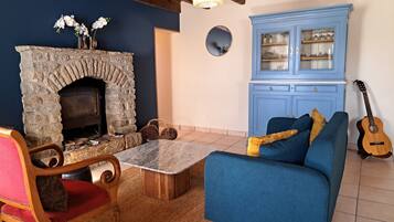 Una sala de estar acogedora con chimenea de piedra, un sofá azul, una silla de madera y una guitarra.