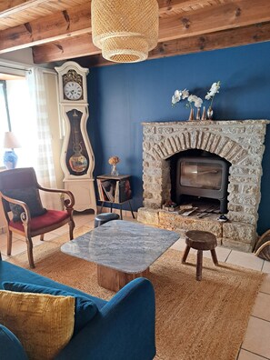 A living room with a stone fireplace, a wooden chair, a blue sofa, and a table. - TyRoch House in Huelgoat, near the forest and lake, in the heart of the Monts d'Arrée, with air conditioning (Huelgoat)