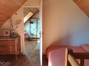Un dormitorio con una cama de madera, un tocador y una silla. Hay una puerta que conduce a un baño con ducha y toallero.