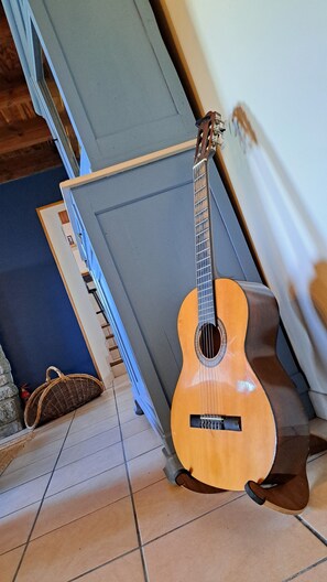 Una guitarra apoyada en una pared, una silla azul y una cesta de mimbre sobre un suelo de baldosas.